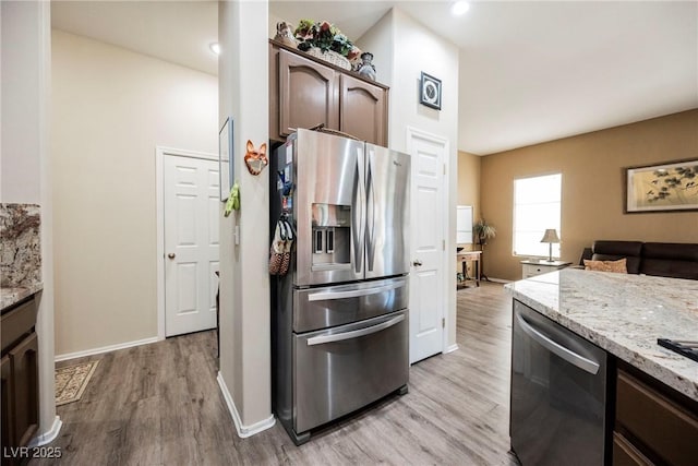 kitchen featuring appliances with stainless steel finishes, dark brown cabinets, light stone counters, and light hardwood / wood-style floors