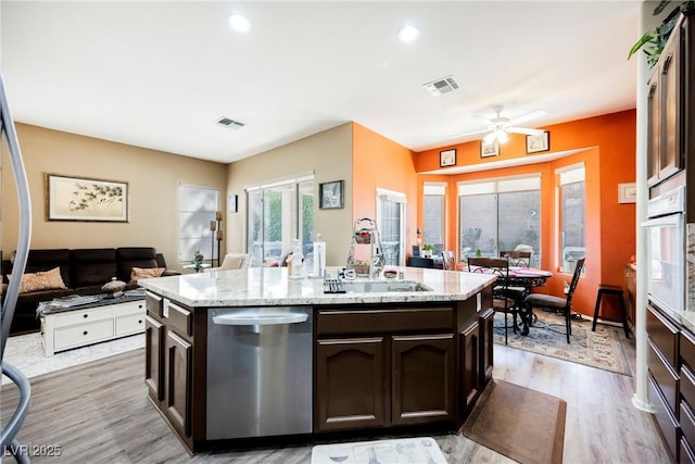 kitchen featuring sink, a kitchen island with sink, dark brown cabinetry, light hardwood / wood-style floors, and stainless steel dishwasher