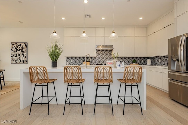 kitchen with stainless steel refrigerator with ice dispenser, white cabinetry, hanging light fixtures, a center island with sink, and a kitchen breakfast bar