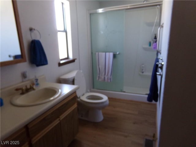 bathroom with vanity, hardwood / wood-style floors, a shower with door, and toilet