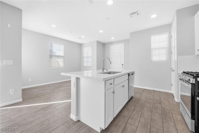 kitchen with stainless steel appliances, sink, white cabinetry, an island with sink, and a healthy amount of sunlight