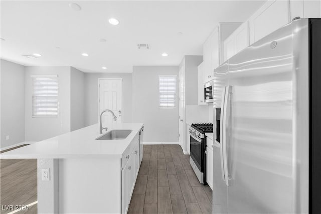 kitchen with white cabinetry, appliances with stainless steel finishes, sink, and a center island with sink