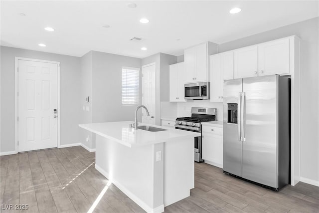 kitchen with sink, white cabinetry, light wood-type flooring, appliances with stainless steel finishes, and an island with sink