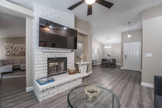 living room with lofted ceiling, a brick fireplace, ceiling fan with notable chandelier, and hardwood / wood-style floors