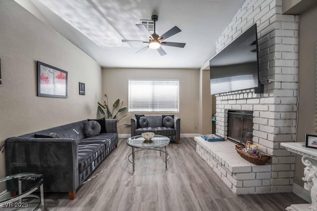 living room featuring a brick fireplace, wood-type flooring, and ceiling fan