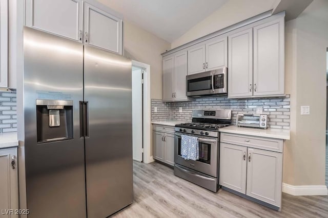 kitchen with stainless steel appliances, gray cabinets, light wood-type flooring, and backsplash