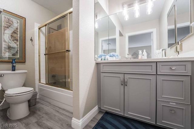 full bathroom with hardwood / wood-style flooring, vanity, shower / bath combination with glass door, and toilet