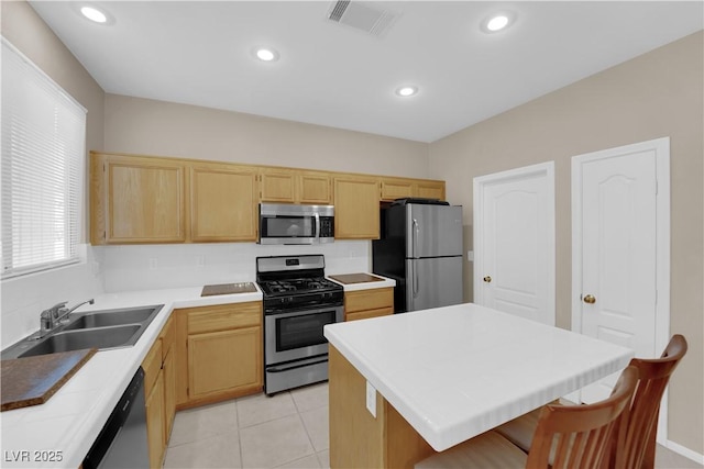 kitchen featuring light tile patterned flooring, appliances with stainless steel finishes, light brown cabinetry, sink, and a center island