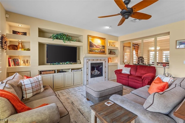 living room with ceiling fan, a stone fireplace, and built in features