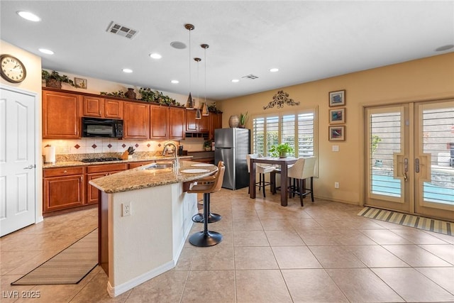 kitchen with sink, hanging light fixtures, a kitchen breakfast bar, black appliances, and an island with sink