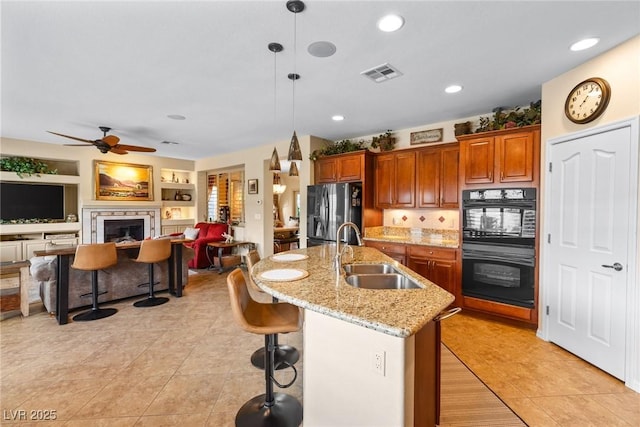 kitchen with pendant lighting, sink, a kitchen bar, black appliances, and a center island with sink