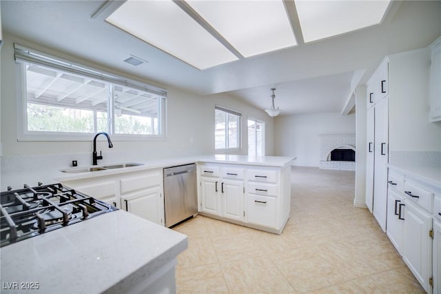 kitchen with a fireplace, dishwasher, sink, white cabinets, and kitchen peninsula