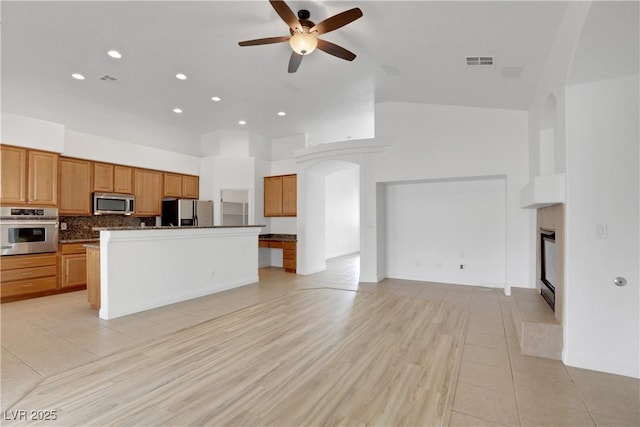 kitchen featuring stainless steel appliances, a center island, a high ceiling, light tile patterned flooring, and decorative backsplash