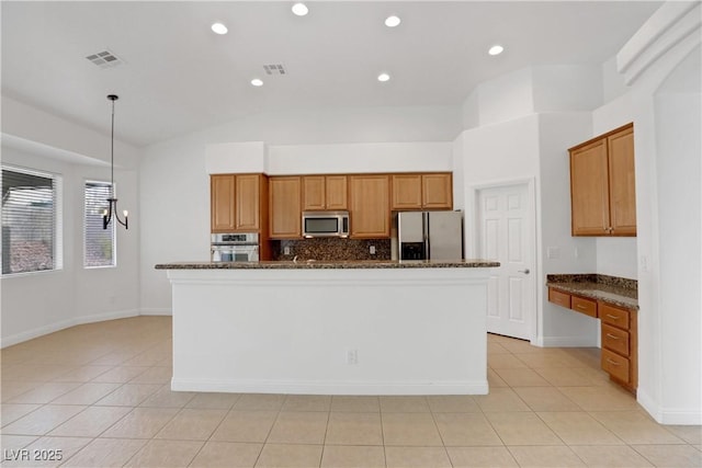 kitchen with built in desk, a center island with sink, dark stone countertops, appliances with stainless steel finishes, and pendant lighting