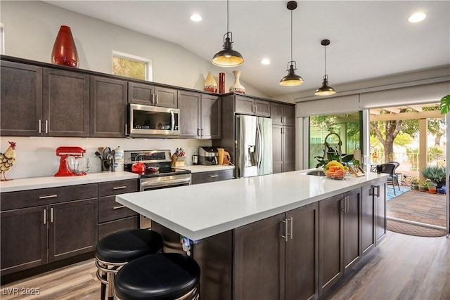 kitchen with a kitchen island with sink, dark brown cabinets, stainless steel appliances, and a breakfast bar