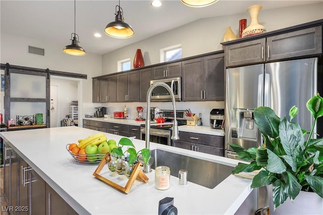 kitchen featuring a barn door, appliances with stainless steel finishes, dark brown cabinets, and pendant lighting