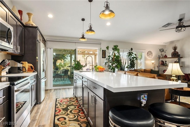 kitchen with pendant lighting, sink, dark brown cabinetry, stainless steel appliances, and a center island with sink