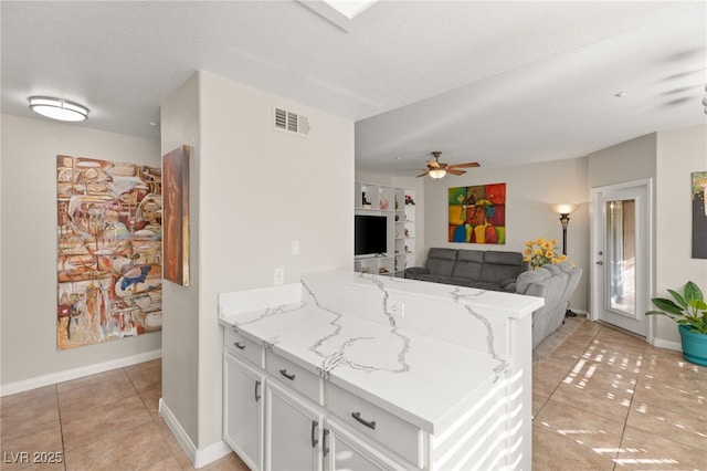 kitchen featuring light stone counters, light tile patterned floors, kitchen peninsula, and white cabinets