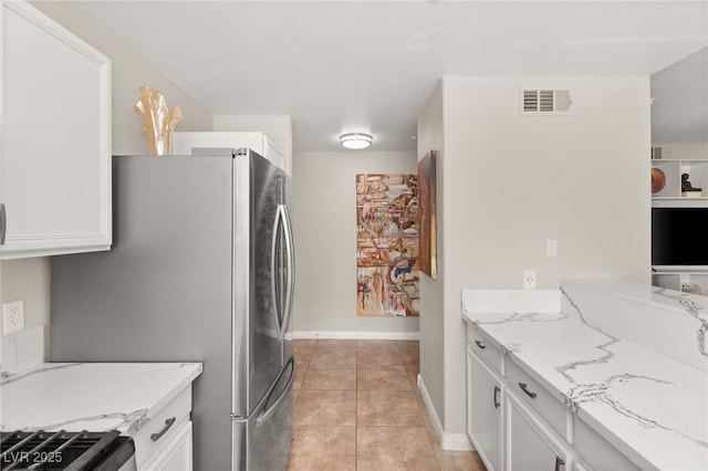 kitchen featuring light tile patterned flooring, stainless steel refrigerator, light stone countertops, and white cabinets