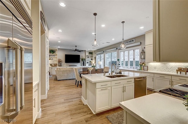 kitchen with decorative light fixtures, dishwasher, an island with sink, sink, and light hardwood / wood-style flooring