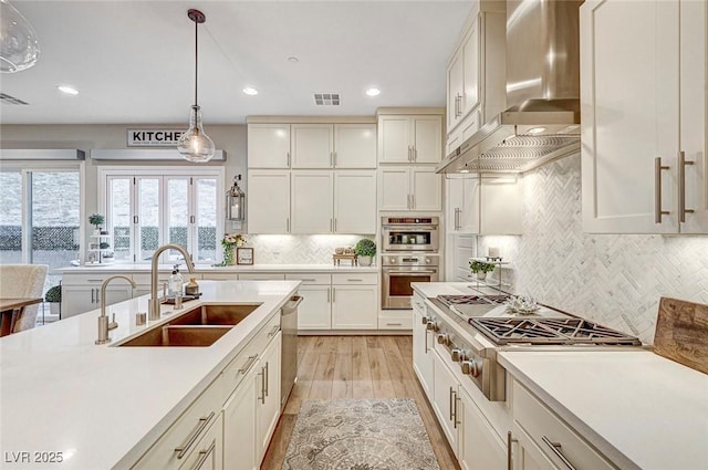 kitchen with decorative light fixtures, sink, backsplash, stainless steel appliances, and wall chimney exhaust hood