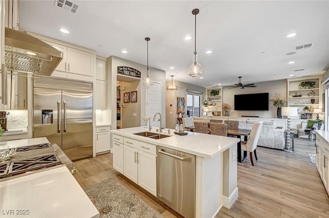 kitchen featuring sink, appliances with stainless steel finishes, an island with sink, pendant lighting, and wall chimney range hood