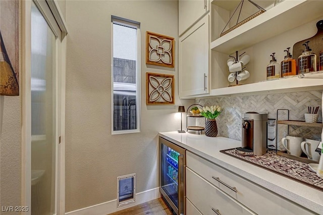 bar featuring tasteful backsplash, beverage cooler, light wood-type flooring, and white cabinets