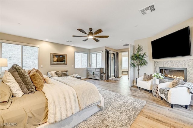 bedroom featuring light hardwood / wood-style flooring, a tile fireplace, and ceiling fan