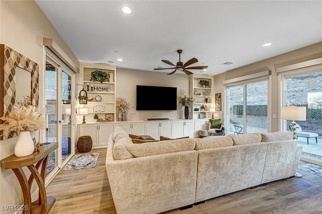 living room featuring ceiling fan, light hardwood / wood-style floors, and built in features