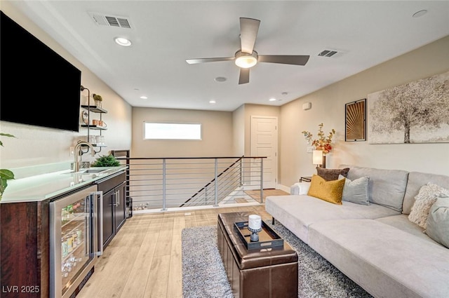 living room with ceiling fan, beverage cooler, light hardwood / wood-style floors, and indoor wet bar