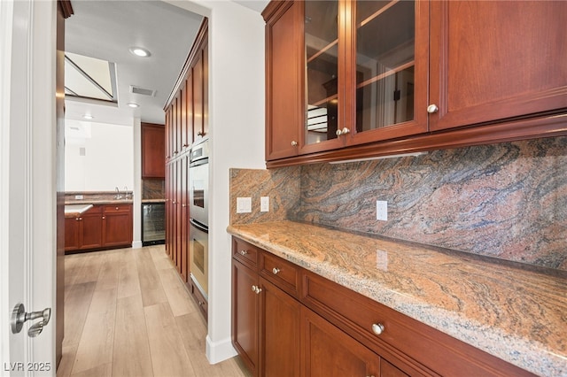 kitchen featuring sink, beverage cooler, backsplash, light stone countertops, and light hardwood / wood-style flooring