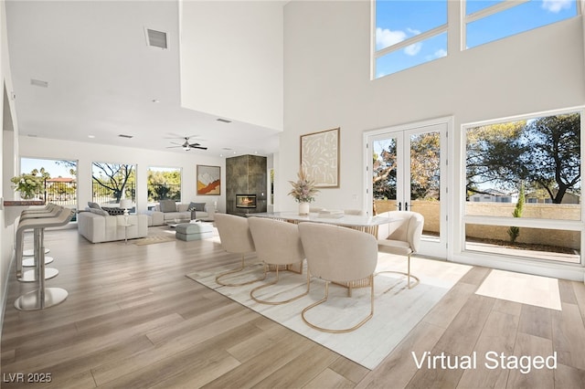 living room featuring a tiled fireplace, french doors, ceiling fan, and light wood-type flooring