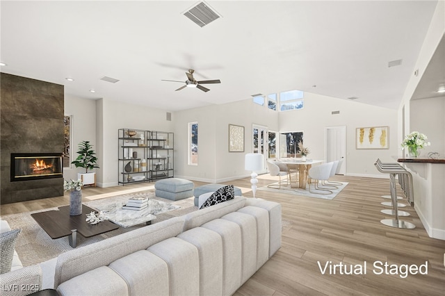 living room with a tiled fireplace, ceiling fan, lofted ceiling, and light hardwood / wood-style floors