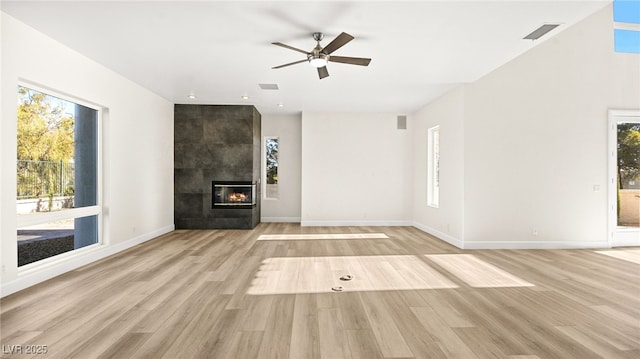 unfurnished living room with a tile fireplace, a wealth of natural light, ceiling fan, and light hardwood / wood-style flooring