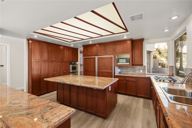 kitchen featuring sink, light stone counters, a center island, light hardwood / wood-style flooring, and appliances with stainless steel finishes