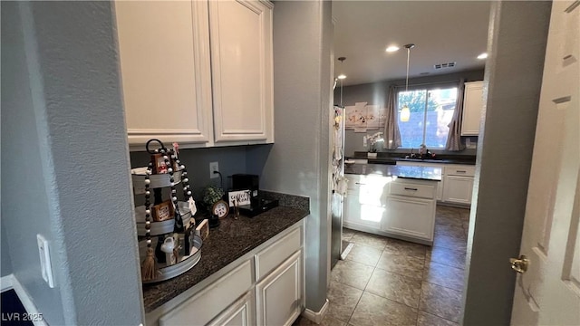 kitchen with sink, white cabinetry, tile patterned flooring, decorative light fixtures, and dark stone counters