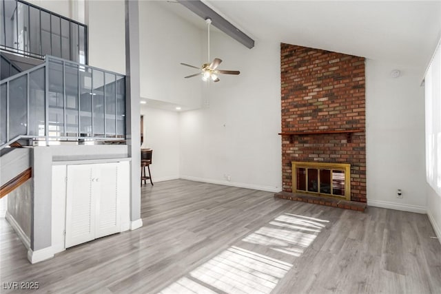 unfurnished living room with beam ceiling, high vaulted ceiling, ceiling fan, a fireplace, and light hardwood / wood-style floors