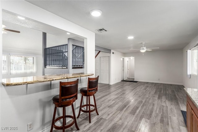 kitchen featuring light stone counters, wood-type flooring, a breakfast bar, and ceiling fan