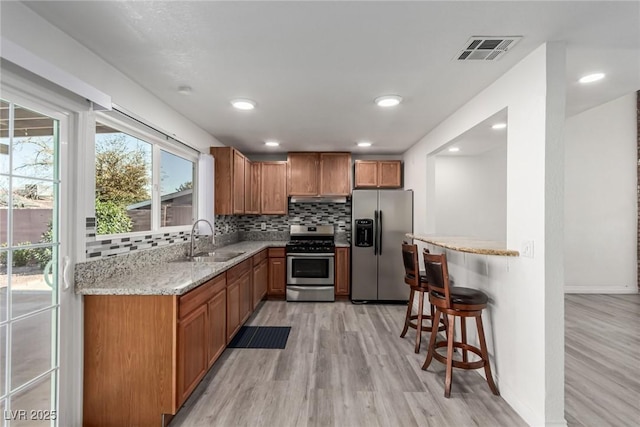 kitchen featuring sink, a breakfast bar area, backsplash, light stone counters, and stainless steel appliances