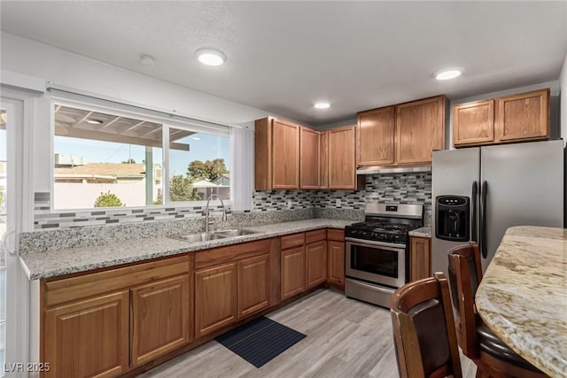 kitchen featuring sink, backsplash, light stone counters, stainless steel appliances, and light wood-type flooring