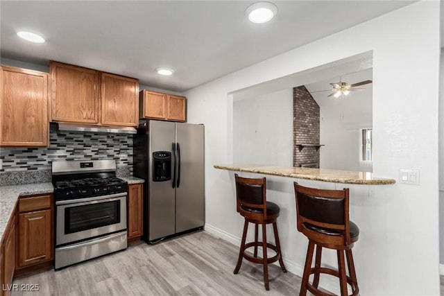 kitchen featuring a kitchen bar, light stone counters, tasteful backsplash, appliances with stainless steel finishes, and kitchen peninsula