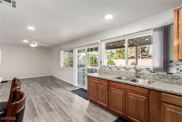 kitchen with sink, ceiling fan, light stone countertops, light hardwood / wood-style floors, and backsplash