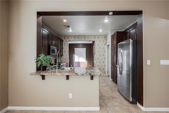 kitchen featuring stainless steel appliances, sink, light stone counters, and kitchen peninsula