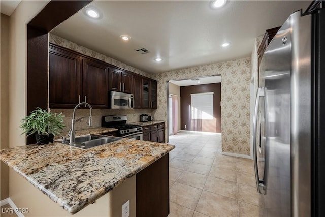 kitchen with appliances with stainless steel finishes, kitchen peninsula, sink, dark brown cabinetry, and light stone counters