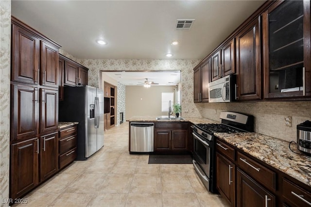 kitchen featuring sink, dark brown cabinets, stainless steel appliances, light stone counters, and kitchen peninsula