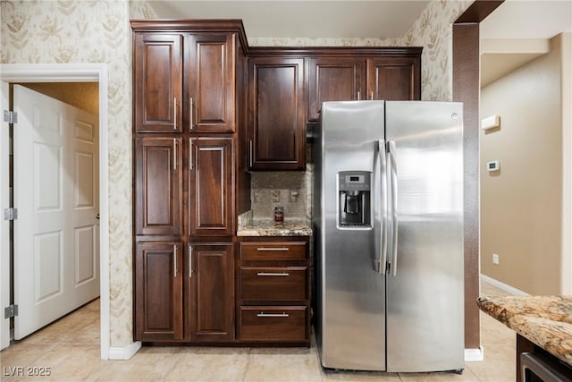 kitchen featuring dark brown cabinetry, stainless steel fridge with ice dispenser, light tile patterned floors, and light stone countertops