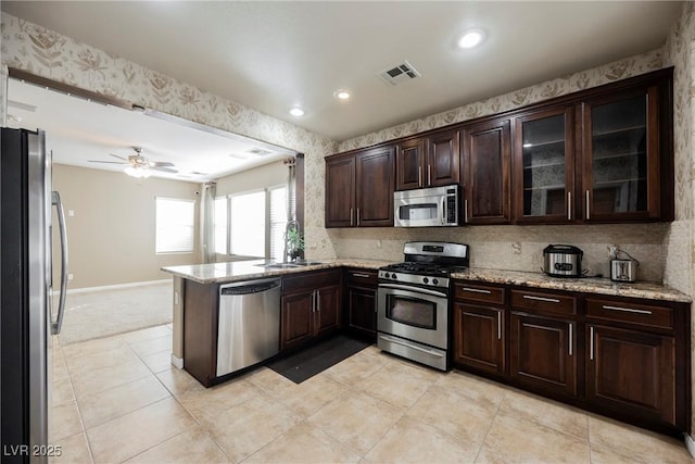 kitchen with light stone countertops, dark brown cabinets, stainless steel appliances, and kitchen peninsula