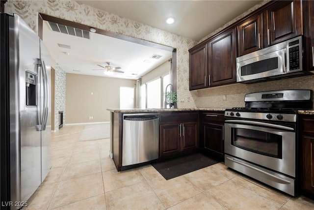 kitchen featuring appliances with stainless steel finishes, light tile patterned floors, light stone counters, kitchen peninsula, and dark brown cabinets