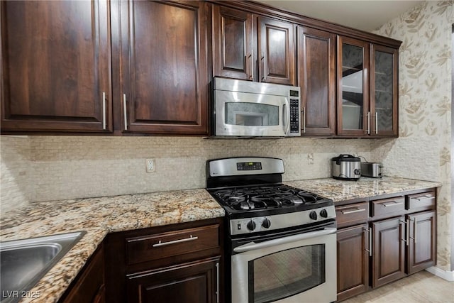 kitchen with stainless steel appliances, light stone countertops, sink, and dark brown cabinetry