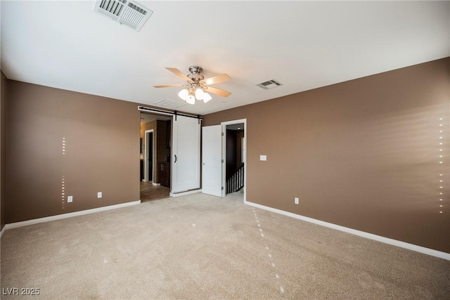 unfurnished bedroom featuring a barn door, ceiling fan, and carpet flooring